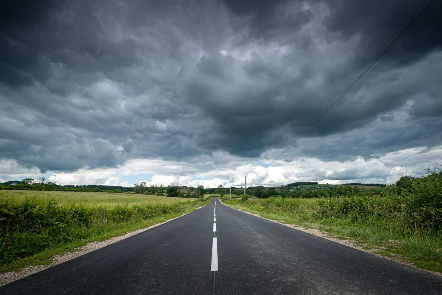 bella vista di una strada vuota circondata dal verde sotto nuvole scure di tempesta