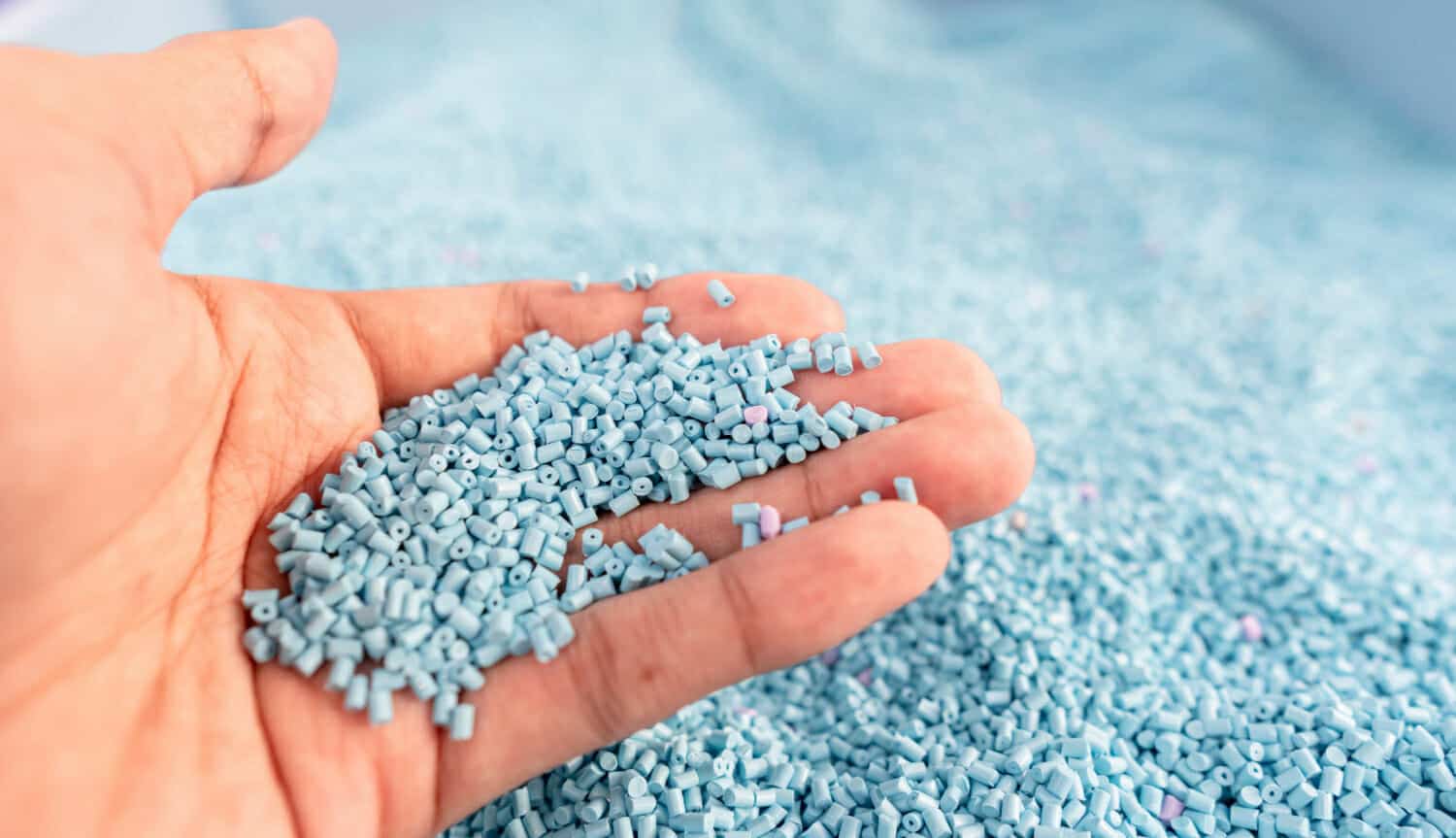 mano su un grande mucchio di granuli di plastica blu in deposito temporaneo della linea di produzione in fabbrica di riciclo pellet di resina plastica polimerica colorante master batch