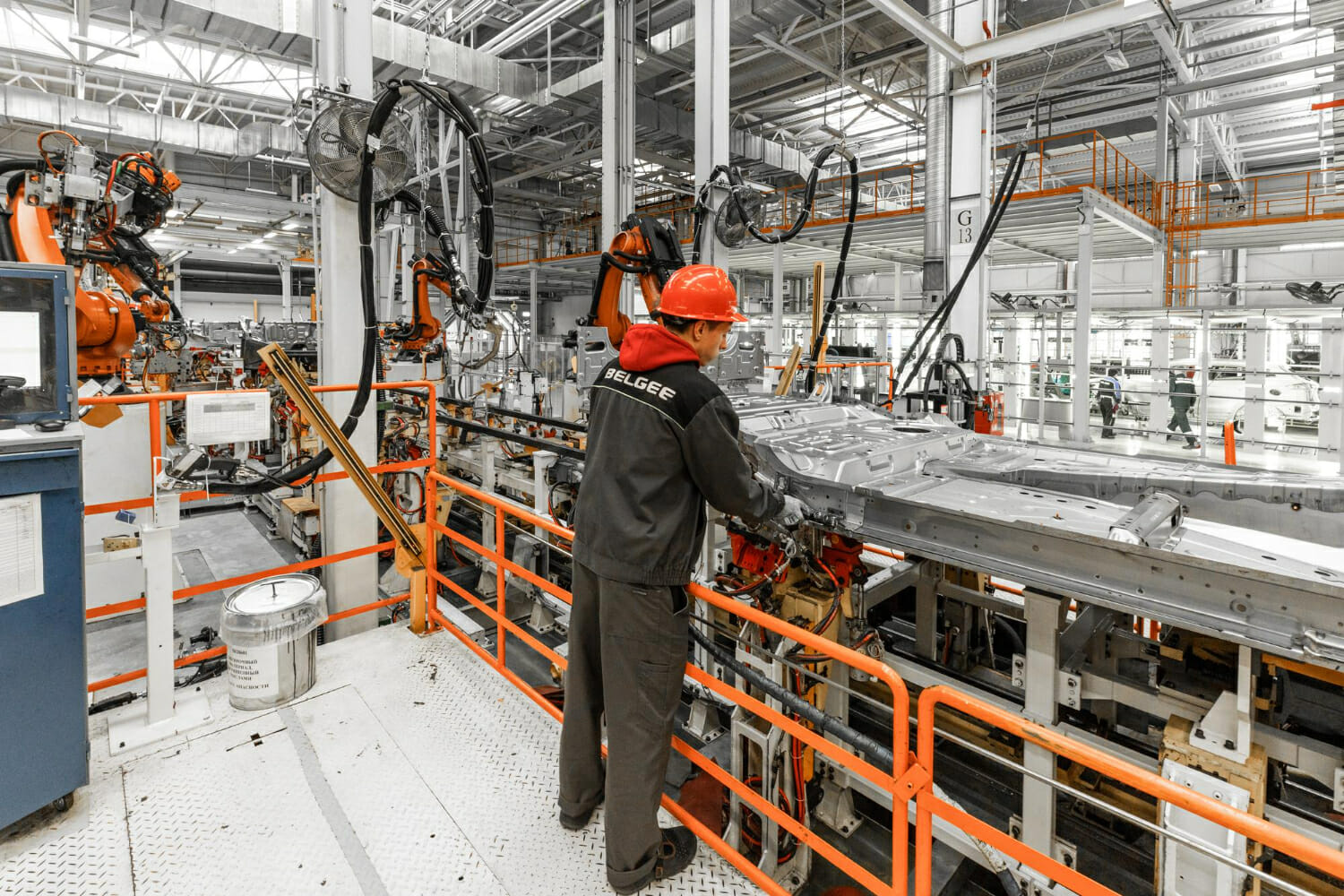 foto della linea di produzione di automobili saldatura di carrozzerie impianto di assemblaggio di automobili moderne industria automobilistica lavoratore maschio in un casco protettivo arancione