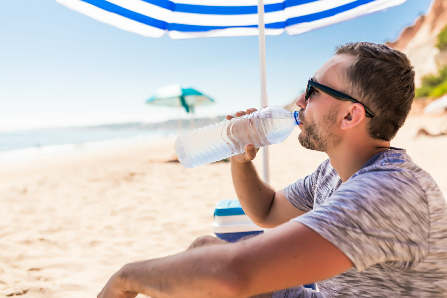 il giovane sotto l ombrello solare verde beve l acqua sulla spiaggia