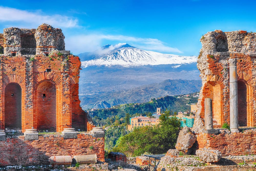 rovine dell antico teatro greco a taormina e il vulcano etna sullo sfondo costa della baia di giardininaxos sicilia italia europa